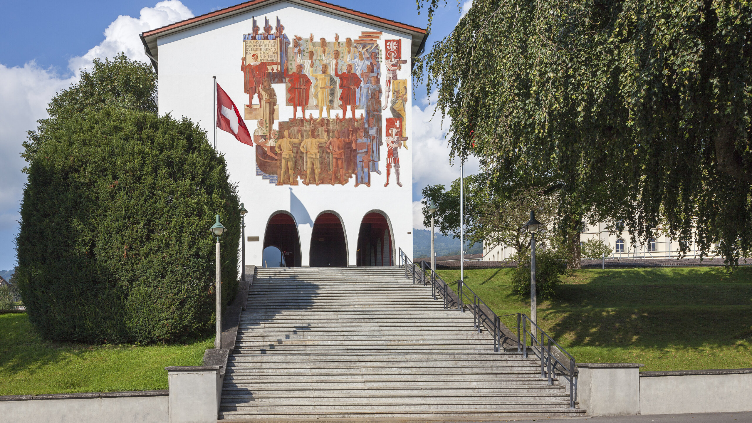 Aussenansicht Bundesbriefmuseum. Eine Freilufttreppe führt zum Eingang hoch. Auf dem Gebäude ist eine Fassadenmalerei, die schwörende Männer zeigt.