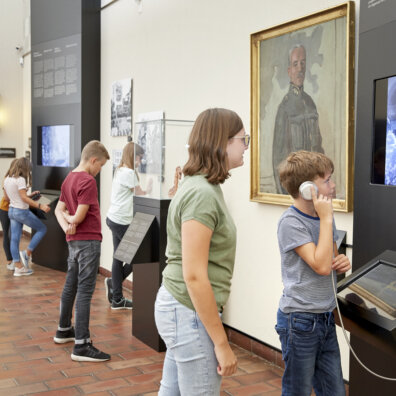 Schülerinnen und Schüler an verschiedenen Stationen im Bundesbriefmuseum. Im Vordergrund hört ein Junge Informationen zu General Guisan und schaut dazu einen Film.