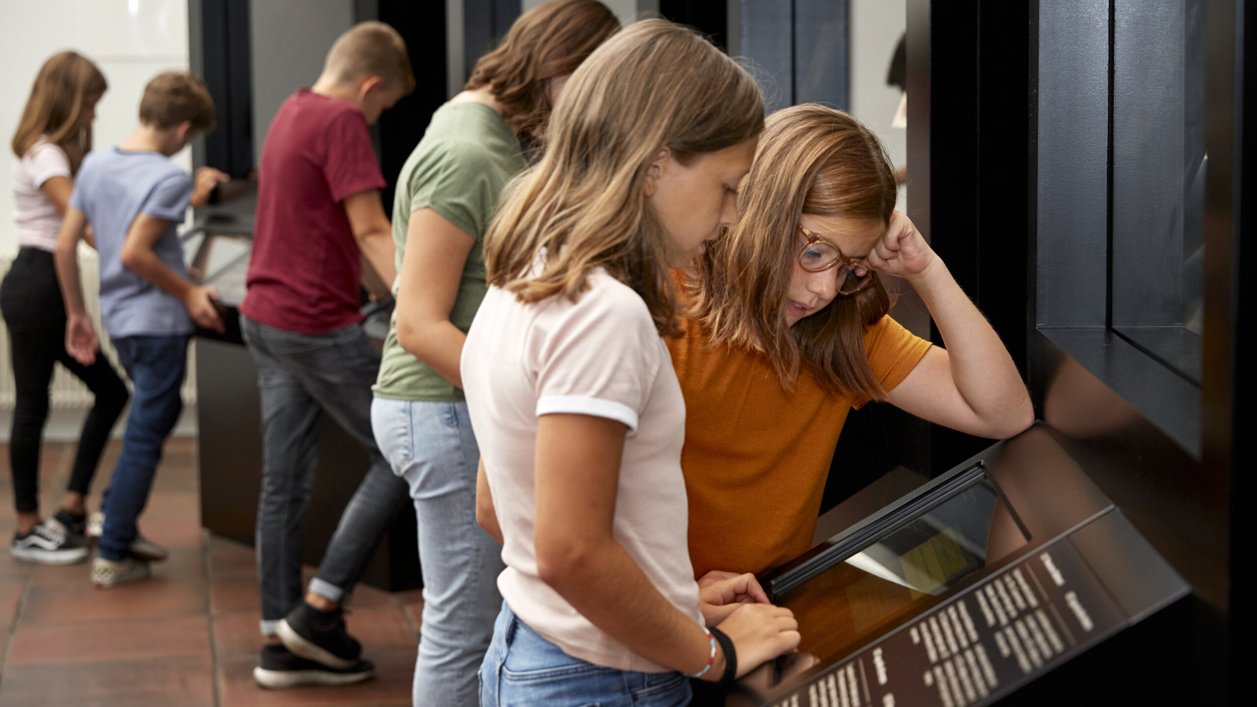 Schülerinnen stehen an einer Ausstellungsstation und schauen ein Exponat an.