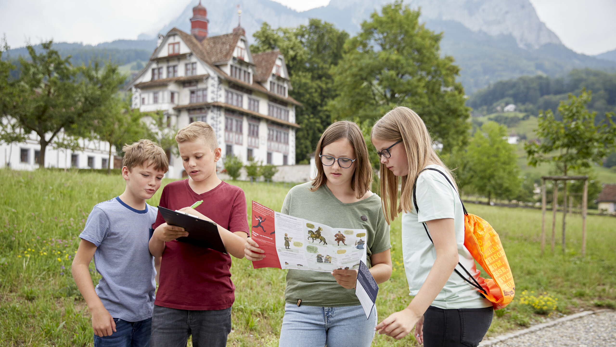 Vier Schülerinnen und Schüler stehen vor der Ital Reding-Hofstatt. Zwei schauen auf den Plan, zwei machen Notizen.