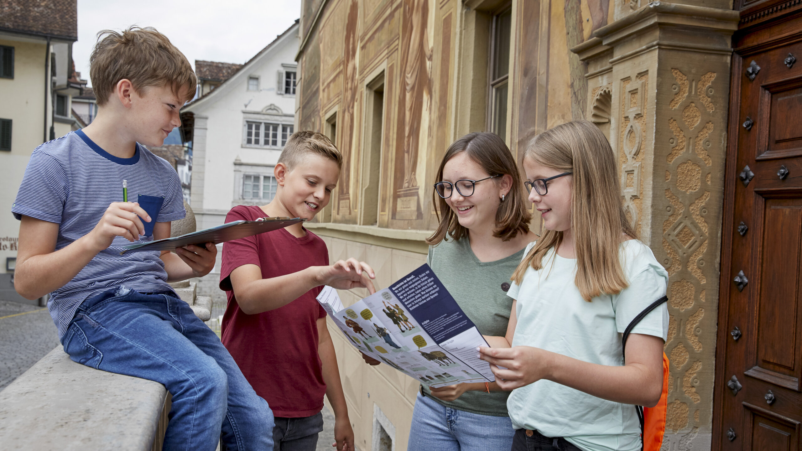 Vier Schülerinnen und Schüler stehen vor dem Rathaus in Schwyz und schauen auf den Orientierungsplan.