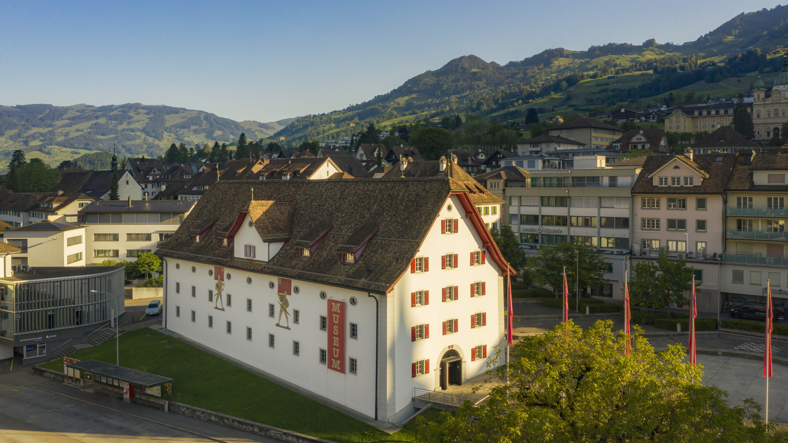 Aussenansicht des Forums Schweizer Geschichte Schwyz. Ein historischer Bau mit roten Fensterläden und zwei Wandmalereien, die Fahnenträger zeigen.