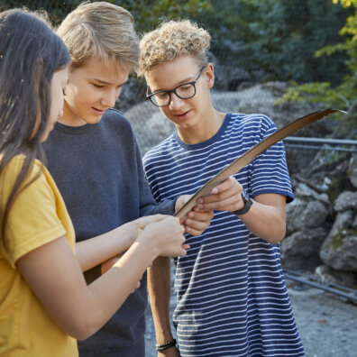 Drei Schülerinnen und Schüler mit einer langen Vogelfeder.