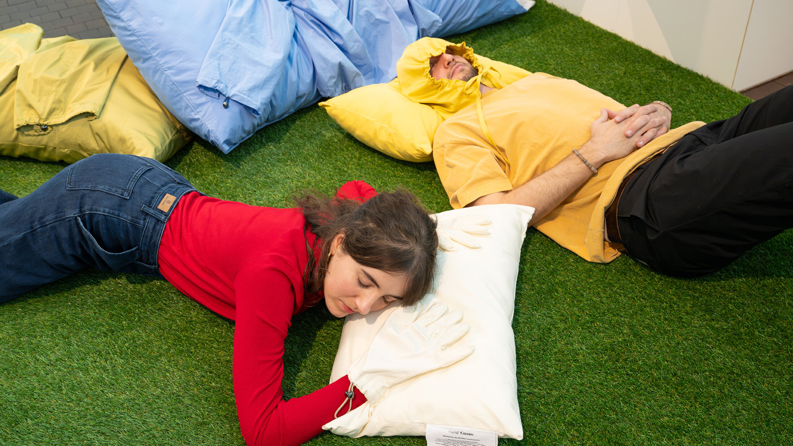 2 Ausstellungsbesucher der Ausstellung Langeweile im Vögele Kultur Zentrum probieren eine Mitmachstation aus. Sie liegen auf speziellen Kissen auf einem Rasenteppich.
